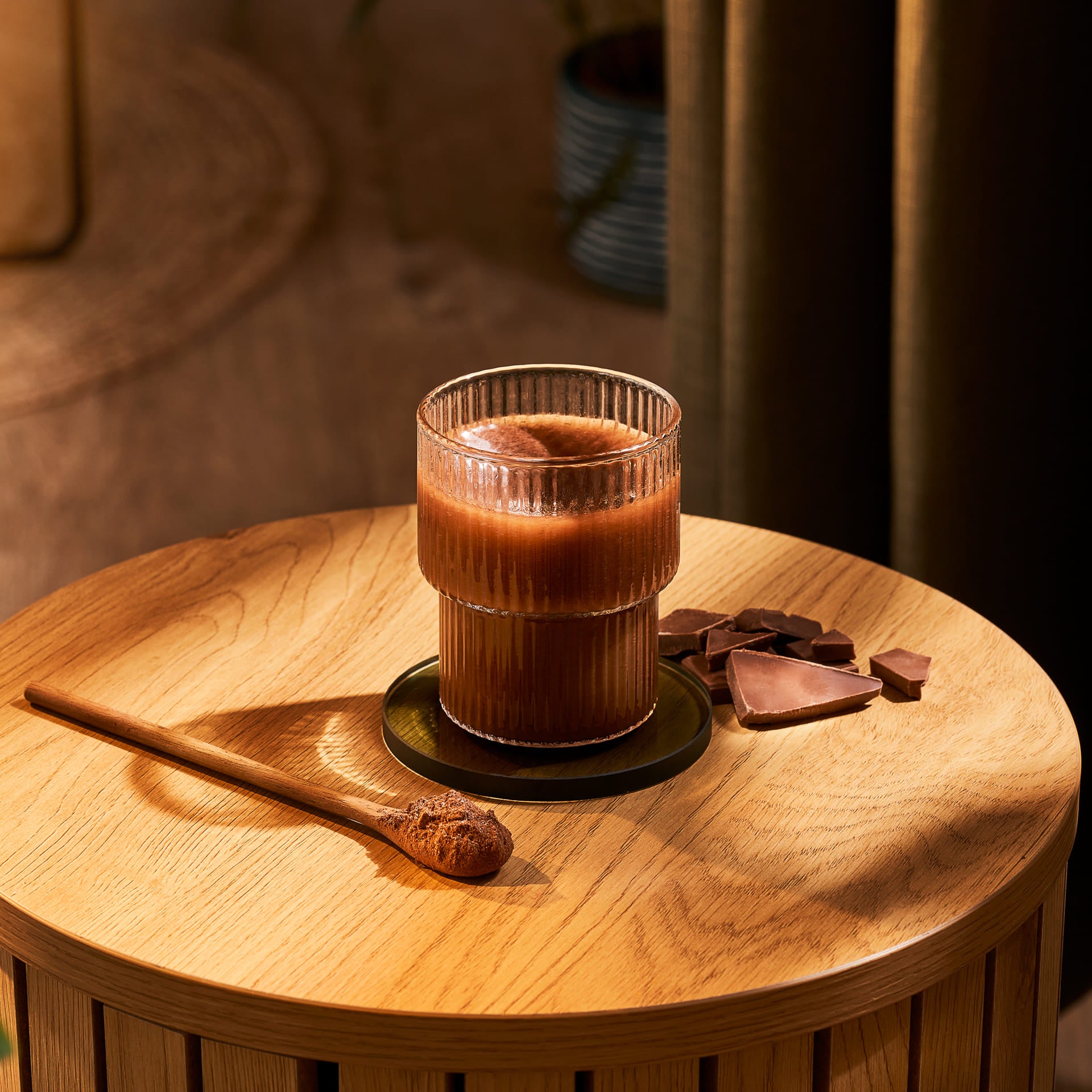 Glass of chocolate milk on a coffee table with a spoon of cacao powder next to it